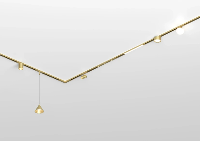 Brass magnetic track turning a sharp V across a white ceiling, carrying spots, a round downlight, a globe and a cone pendant