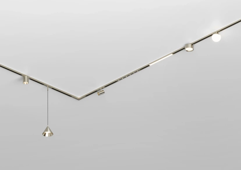 Nickel-finish magnetic track turning a sharp V across a white ceiling, carrying spots, a round downlight, a globe and a cone pendant