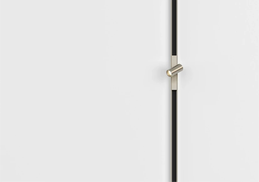 A vertical nickel-finish magnetic track running down a white wall with a single adjustable spot